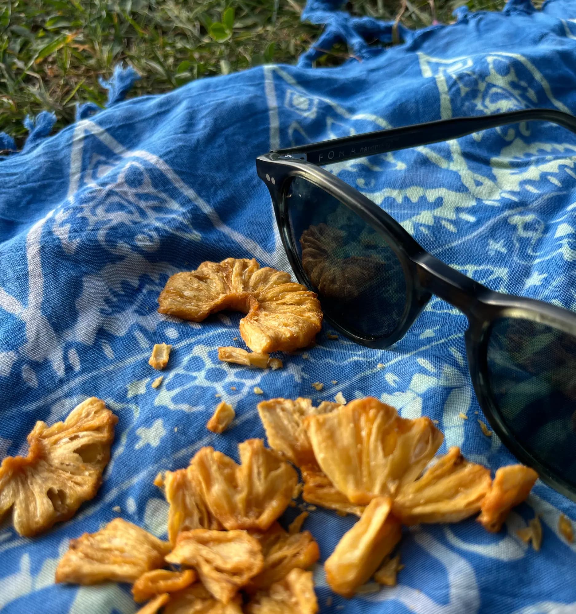 Nahaufnahme goldener Crispy-Ananas-Stücke auf einer blauen Picknickdecke, daneben eine Sonnenbrille